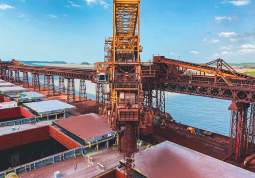 Iron ore conveyor loading cargo in the bulk carrier with a cloudy blue sky in the background